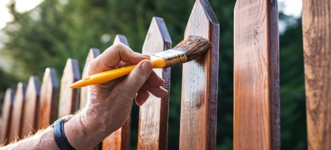 hand brushing stain onto wood fence