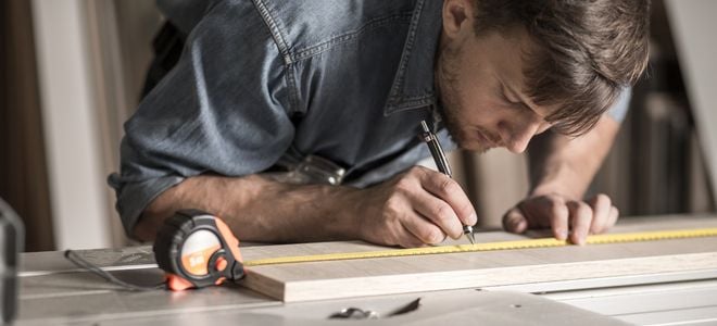 person carefully measuring line on piece of wood