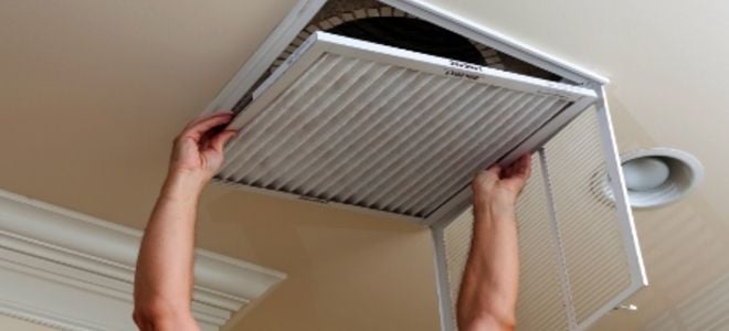 A man replacing the filter in a ceiling vent. 