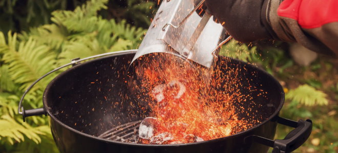 gloved hand pouring lit coals into grill