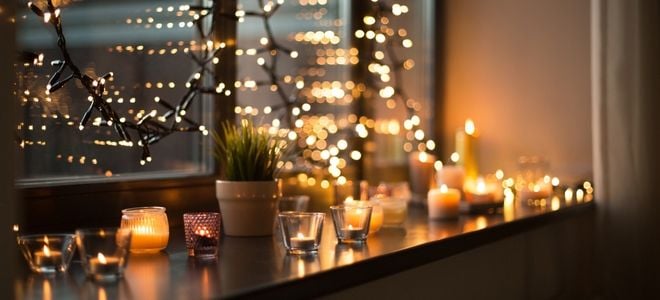 a string of lights with candles and a plant by an inside window in a city