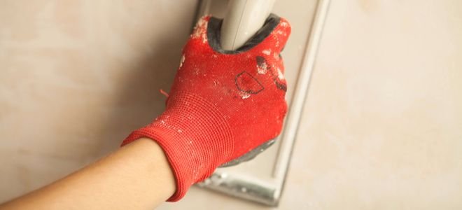 gloved hand sanding wall with tool