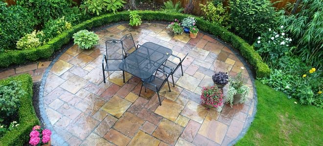 wet circular flagstone patio with metal furniture surrounded by low hedges and lawn