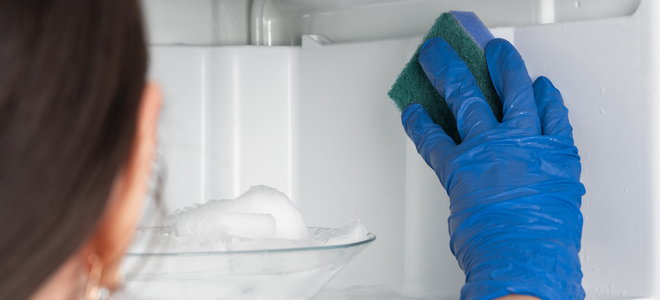 woman cleaning freezer with glove and sponge