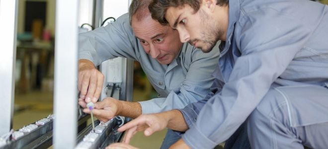 young man learning trade skill from older man 