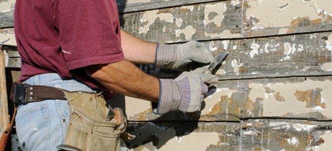 gloved hands scraping wood siding