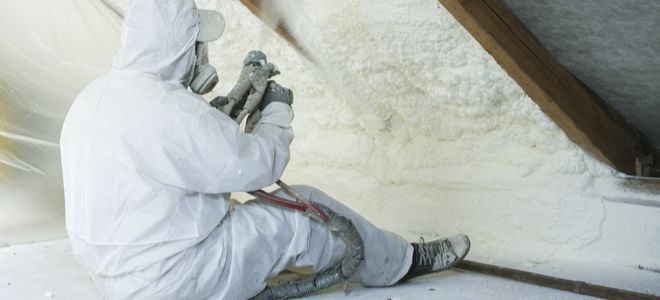 person in protective gear spraying insulation on a ceiling
