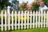An old, white picket fence surrounds a yard of flowers.