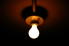 A lone, exposed light bulb hanging from a fixture on the ceiling and illuminating an otherwise-pitch-black room.