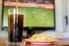 A TV in the background with a football game on, and soda and chips in the foreground. 
