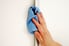 A hand cleaning a white wall with a blue rag. 