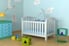 A white baby crib sits in a room with blue walls and a hardwood floor.