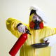 Someone in a yellow suit wearing a chef hat and holding a fire extinguisher and a pan.