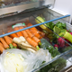 Produce door of refrigerator full of carrots, broccoli and other vegetables