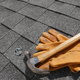 Gloves, a hammer, and roofing nails sit on a shingled roof.