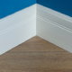 Corner of a room with blue wall, white baseboard trim and wood floors