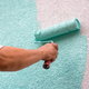 A homeowner painting a teal color over a stuccoed surface.