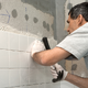 man installing white tile on the wall of a shower