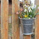 A wooden fence with a bucket of flowers hanging from it.