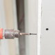 A side profile of a drill inserting a drywall screw into a piece of drywall. 
