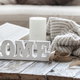 wood block spelling the word "HOME" on a table with book and sweater