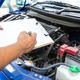 A man holding a checklist looking at a car engine. 