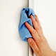 A hand cleaning a white wall with a blue rag. 