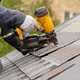 person shingling roof with nail gun