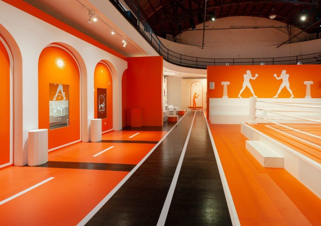 Wide black and orange track runs through a Hermèsfit pop-up gym.