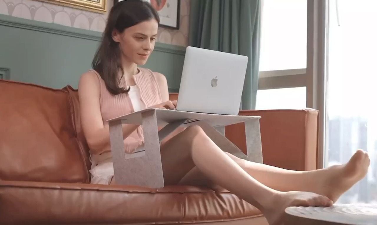 Woman works on her couch with the help of the iSwift M portable laptop desk.