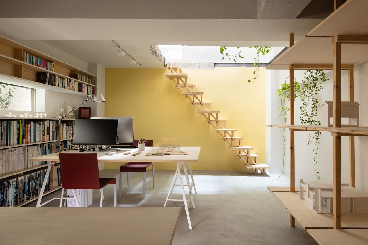 Lower-level office space in the renovated concrete residence is accented by lots of plywood and a bold yellow wall near the stairs. 