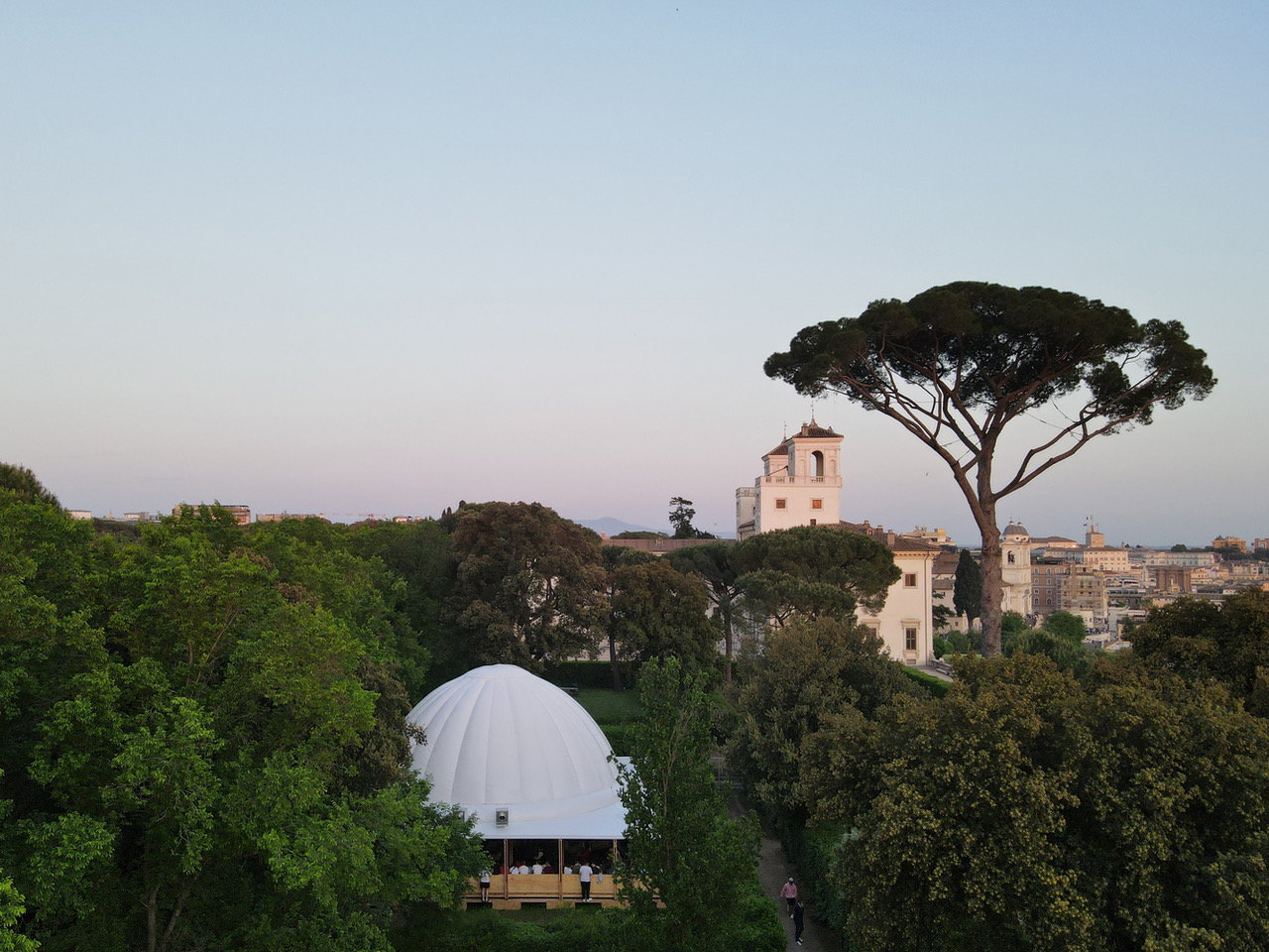 The white canopy of the inflatable ProtoCAMPO pavilion peeks through the trees in Rome