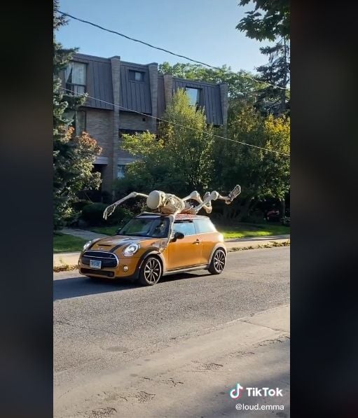 Still from a viral TikTok in which a giant inflatable Home Depot skeleton rides around town on the top of a Mini Cooper.