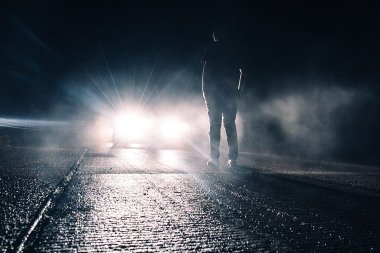 Person in road being blinded by car headlights.