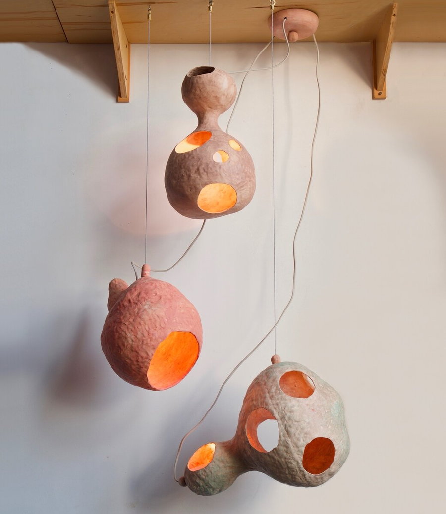 Three of Yuko Nishikawa's handcrafted ceramic lamps hang from a shelf. 