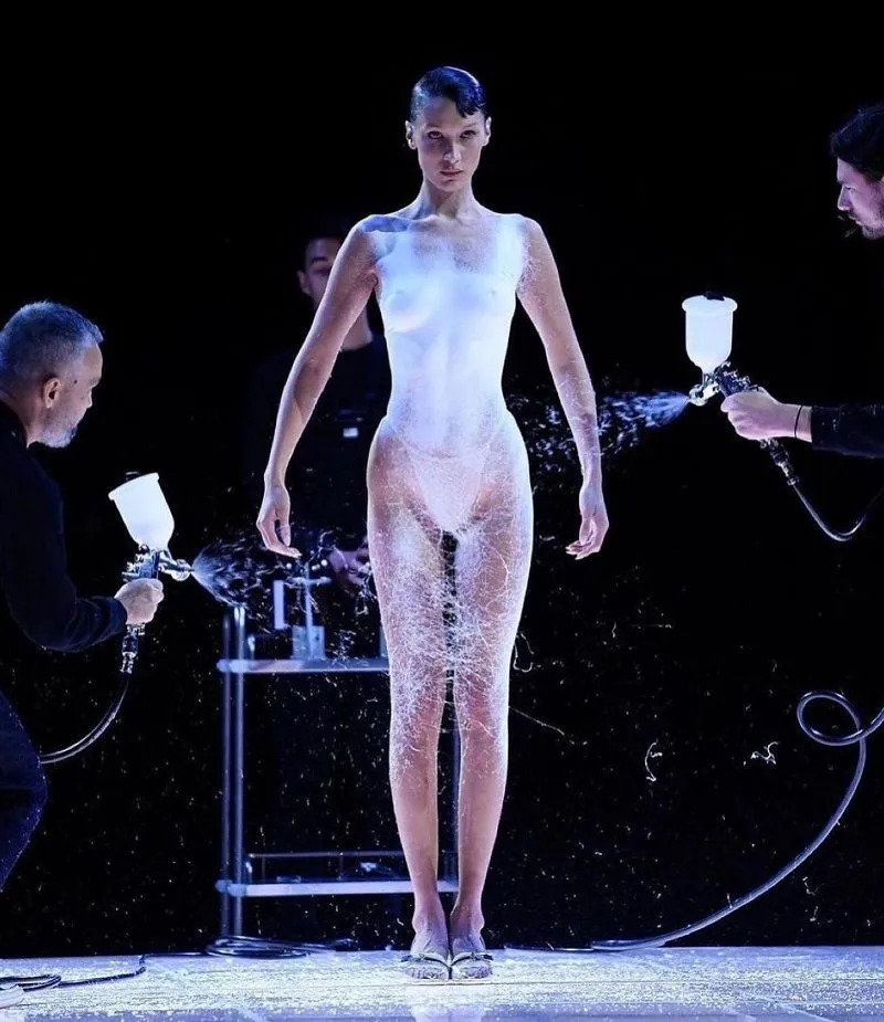 Technicians spray a white Fabrican dress onto Bella Hadid's body at the Coperni fashion show during Paris Fashion Week 2022. 