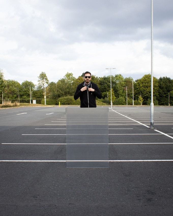 Man holds up a Real Invisibility Shield in a vacant parking lot.