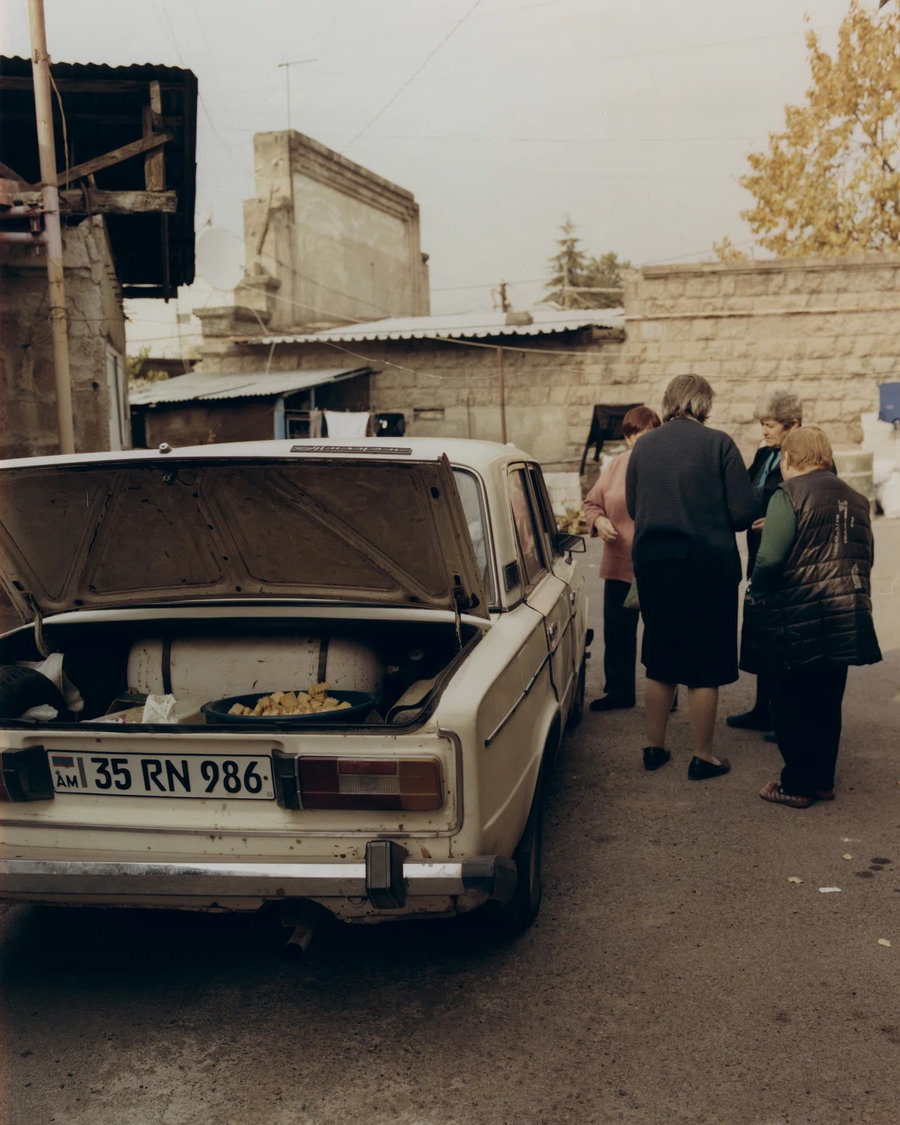 Armenian women sell fruit out of the trunk of a Soviet-era Lada car.