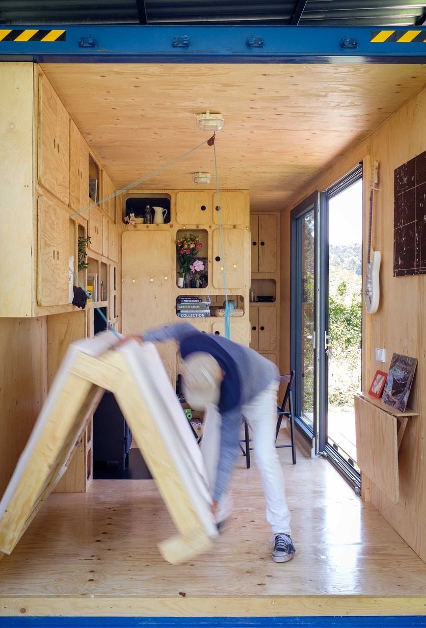 Man pulls out the Gaia Off-Grid Container House's folding bed.