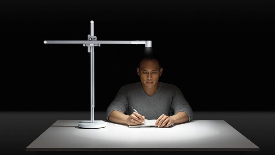 Man writes in a dark room under the bright light of his Dyson Lightcycle.