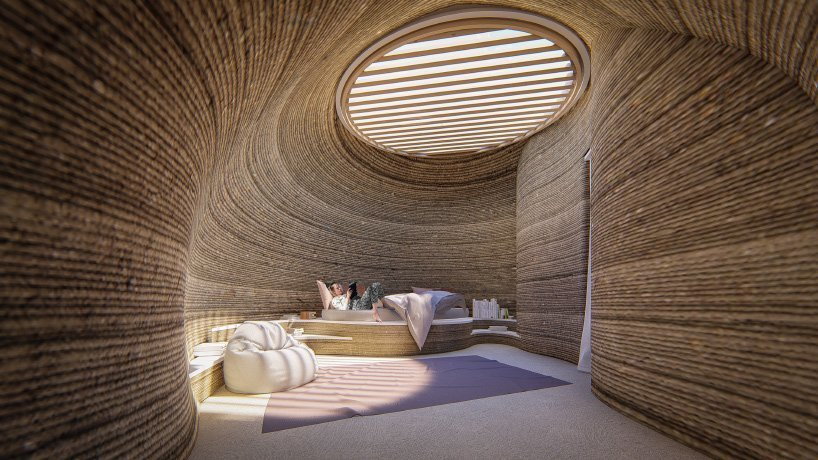 Man reads comfortably on a bed in his raw earth TECLA dome home, with the overhead skylight flooding the interiors with natural light. 