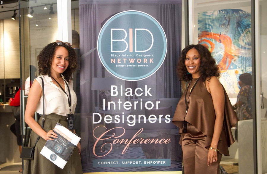 Black Interior Designers Network President Keia McSwain stands in front of a BIDN conference banner. 