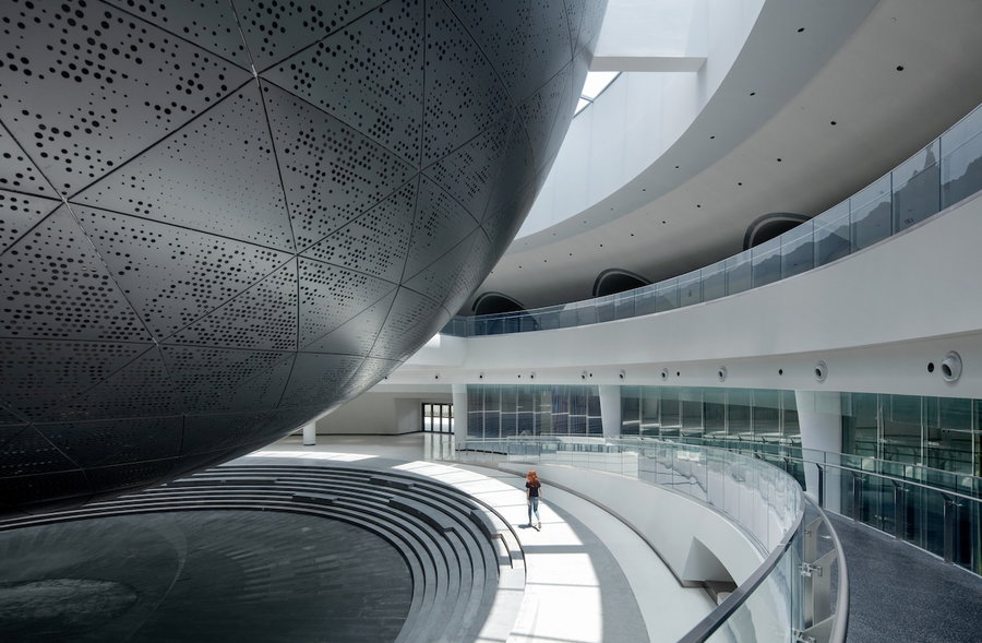 Museum-goer walks alongside the massive suspended planetarium sphere inside the new Shanghai Astronomy Museum.