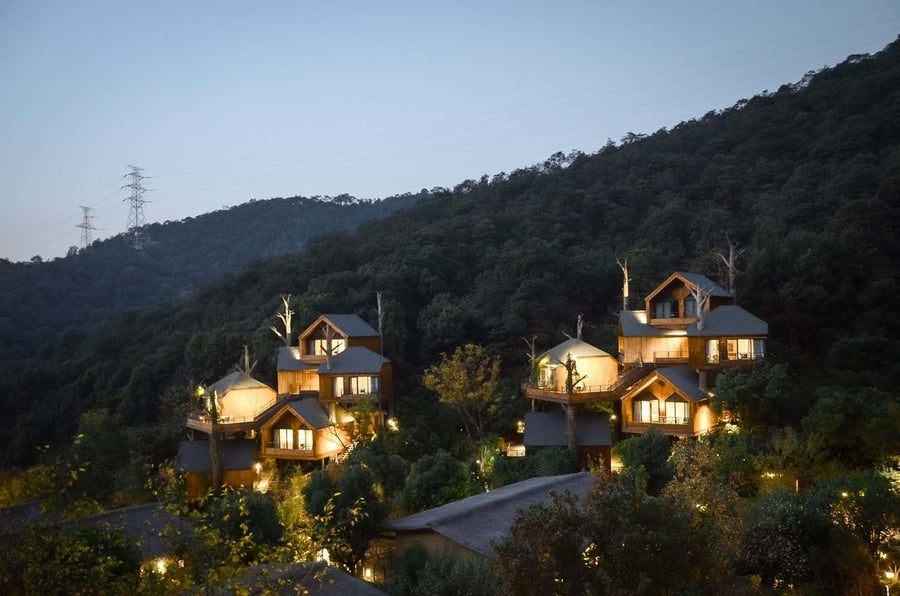 Warm lights inside the stacked treehouse cabins at China's Xiaoshan Xianghu resort glow in the coming dusk.