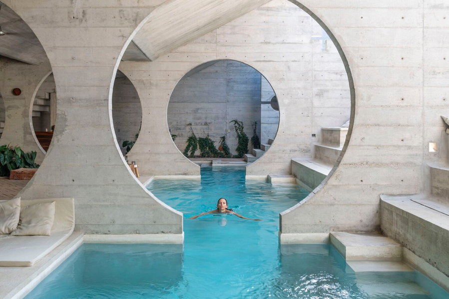 Woman swims through a circular concrete cutout running through the Casa TO's infinity pool.