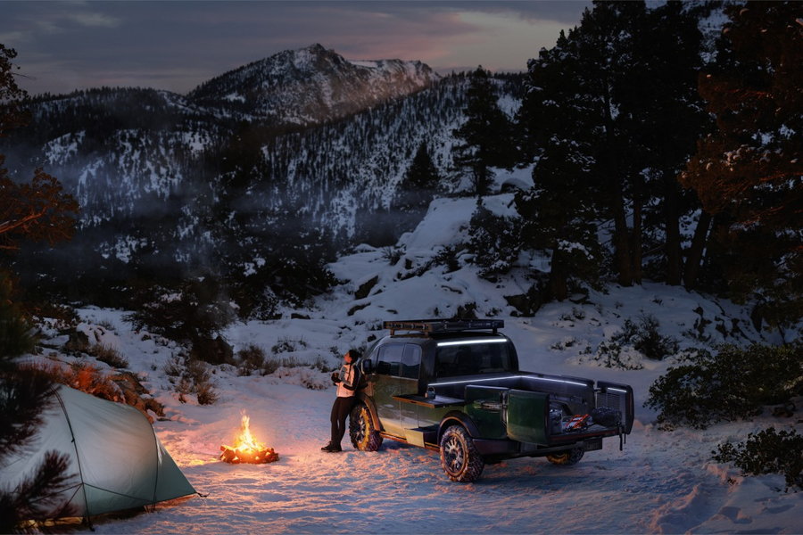 Camper leans on their Canoo electric pickup truck as they gaze up at the stars.