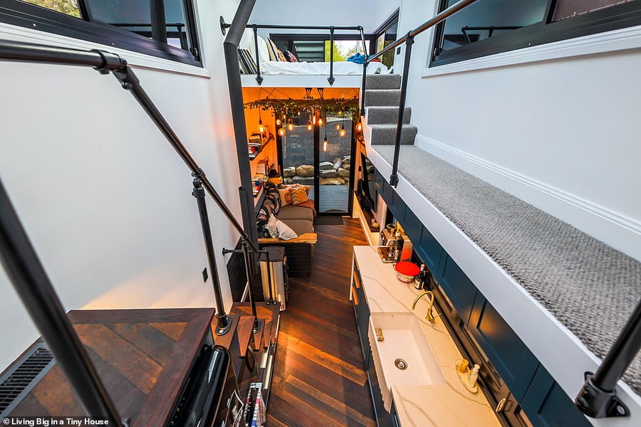 View down at the ultramodern tiny home's minimalist interiors, with a catwalk on the upper level leading to a loft bed on the right.