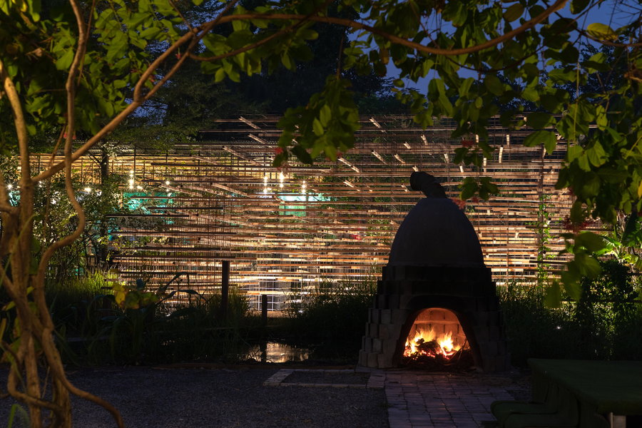A large fireplace glows in front of MIA Design Studio's Straw Pavilion at night.