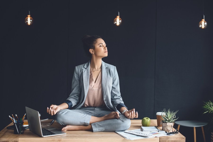 A young woman meditates on her desk at work. 