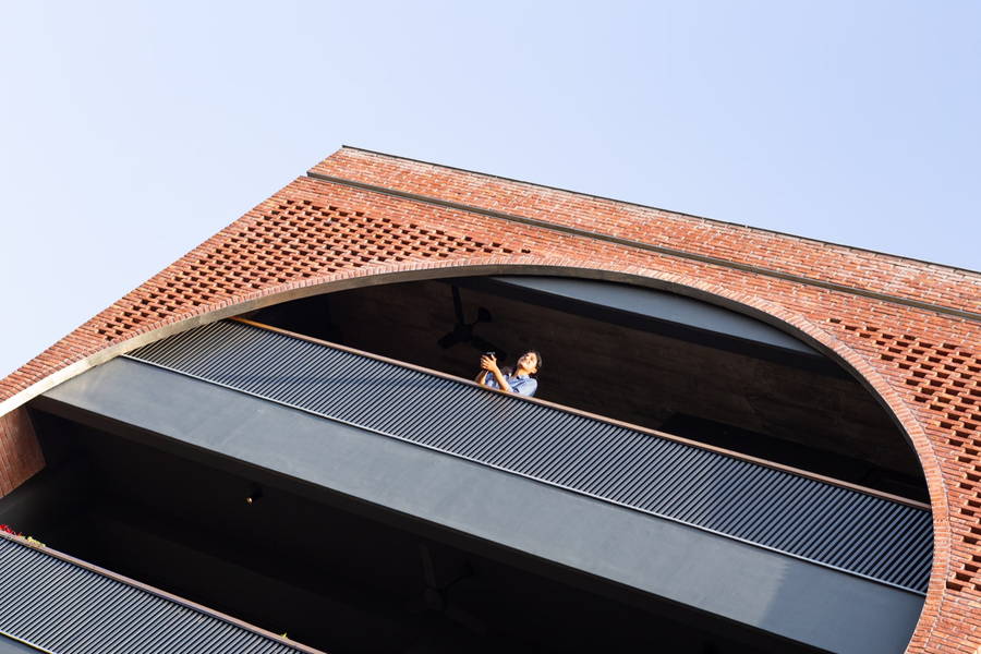 Person leans over the railing of a sleek industrial balcony featured in AKDA's Louis Khan-inspired New Delhi apartment.